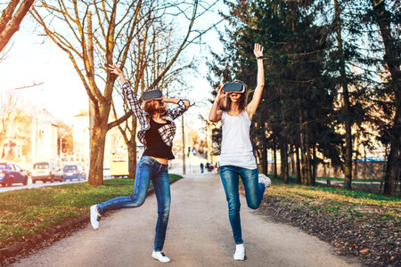 Two young girls enjoy virtual reality glasses outdoor