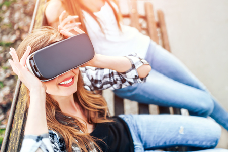 Two young girls enjoy virtual reality glasses outdoorの写真素材