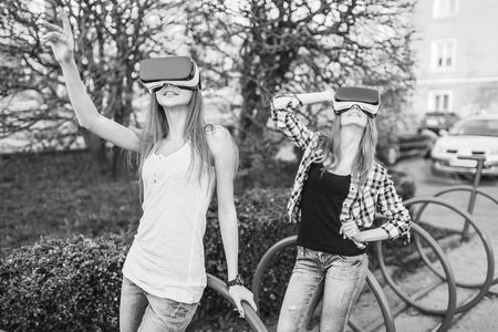 Two young girls enjoy virtual reality glasses outdoor, black and whiteの写真素材