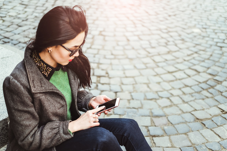 Young brunette girl sitting on the street with cellphoneの写真素材
