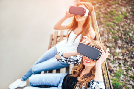 Two young girls enjoy virtual reality glasses outdoorの写真素材