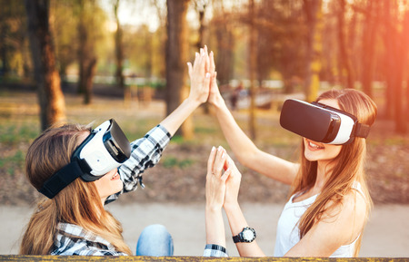 Two young girls enjoy virtual reality glasses outdoorの写真素材