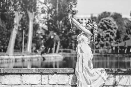 Pretty young bride with wedding bouquet outdoor in the park near lake, black and whiteの写真素材
