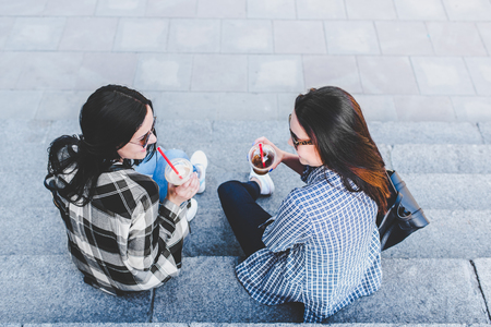 Two pretty brunette girls talking and drinking coffee outdoorの写真素材