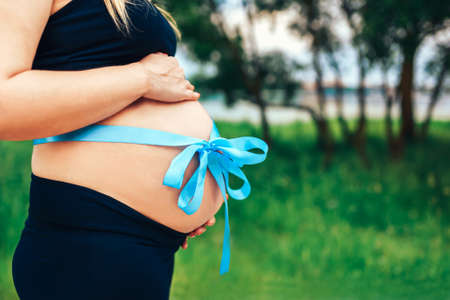 Closeup photo of pregnant woman outdoor with present riband on abdomenの写真素材