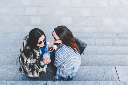 Two pretty brunette girls talking and drinking coffee outdoorの写真素材