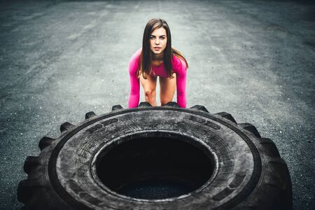 Pretty sporty girl lifting huge tire outdoorの写真素材