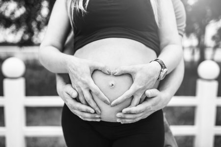Closeup photo of pregnant woman with heart shaped hands on mothers abdomen, black and white