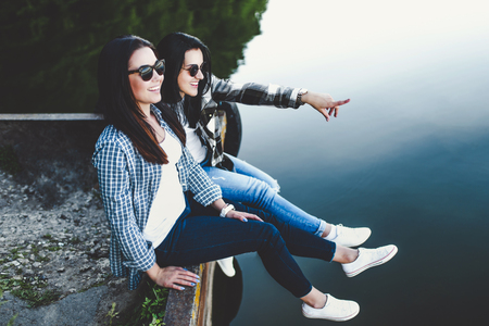 Two pretty brunette girls sitting on the pier near lakeの写真素材