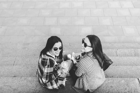 Two pretty brunette girls talking and drinking coffee outdoor, black and whiteの写真素材