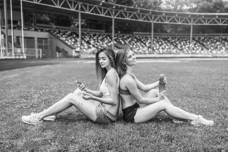 Two pretty sporty girls relaxing after workout outdoor, black and whiteの写真素材