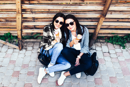 Two pretty girls talking and eating ice cream outdoorの写真素材