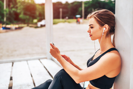 Pretty sporty girl with phone and bottle outdoorの写真素材
