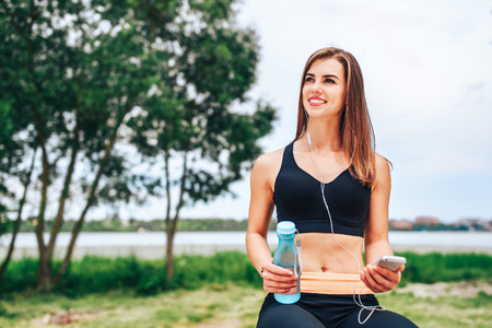 Pretty sporty girl with phone and bottle outdoorの写真素材