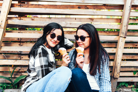 Two pretty girls talking and eating ice cream outdoorの写真素材