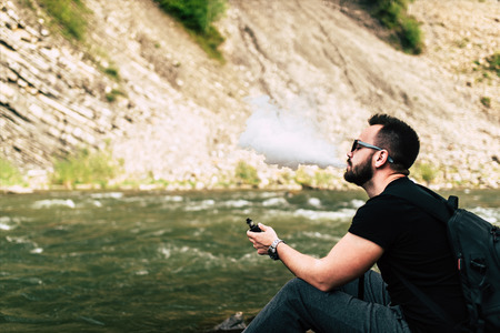 Traveler smoke electronic cigarette near mountain riverの写真素材