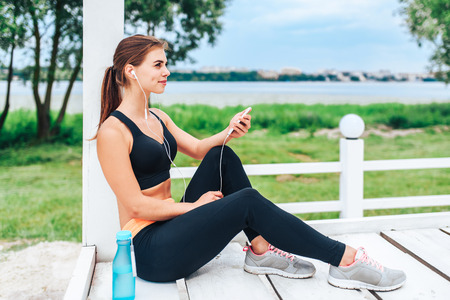 Pretty sporty girl with phone and bottle outdoorの写真素材