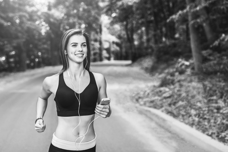 Sporty young fitness girl running and listening music in the park, black and whiteの写真素材