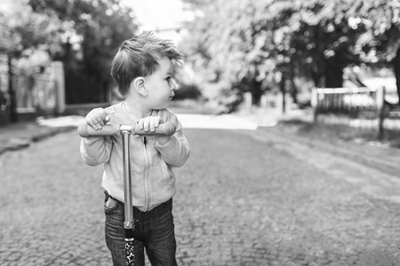Cute little boy riding scooter outdoor on the street, black and whiteの写真素材
