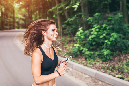 Sporty young fitness girl running and listening music in the parkの写真素材