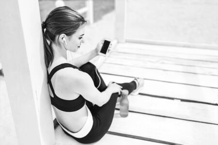 Pretty sporty girl with phone relaxing outdoor after training, black and whiteの写真素材