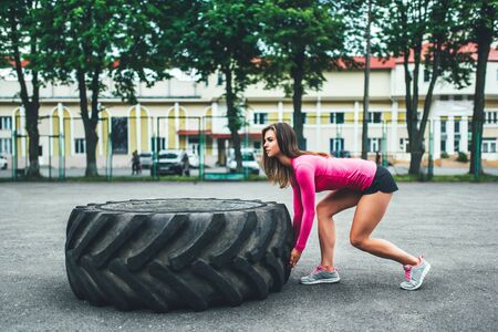 Pretty sporty girl lifting huge tire outdoorの写真素材