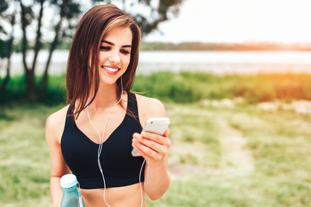 Pretty sporty girl with phone and bottle outdoorの写真素材