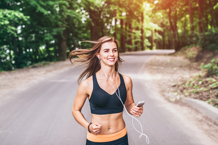 Sporty young fitness girl running and listening music in the parkの写真素材