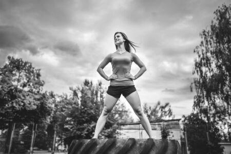 Pretty sporty girl standing on huge tire outdoor, black and whiteの写真素材