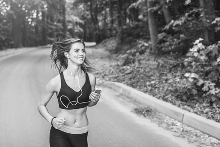 Sporty young fitness girl running and listening music in the park, black and whiteの写真素材