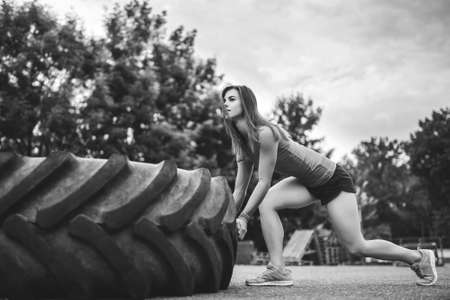 Pretty sporty girl lifting huge tire outdoor, black and whiteの写真素材