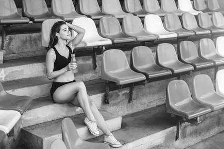 Pretty sporty girl relaxing outdoor after training with bottle of water, black and whiteの写真素材