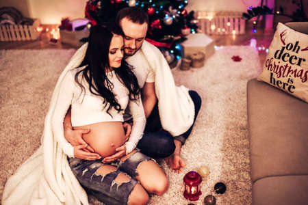 Pregnant mother and her husband at home with christmas decorationsの写真素材