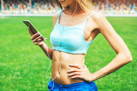 Pretty sporty girl with phone relaxing outdoor after trainingの写真素材
