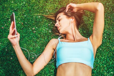 Pretty sporty girl with phone relaxing outdoor after trainingの写真素材
