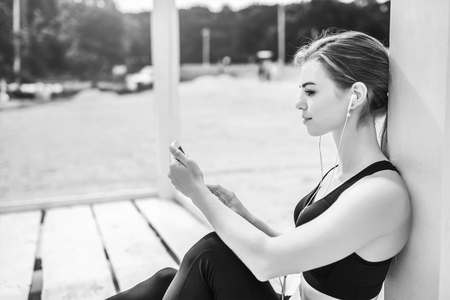 Pretty sporty girl with phone relaxing outdoor after training, black and whiteの写真素材