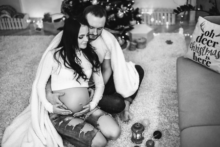 Happy pregnant woman with husband at home with christmas decorationsの写真素材