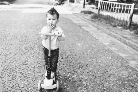 Cute little boy riding scooter outdoor on the street, black and whiteの写真素材