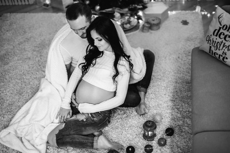 Happy pregnant woman with husband at home with christmas decorationsの写真素材