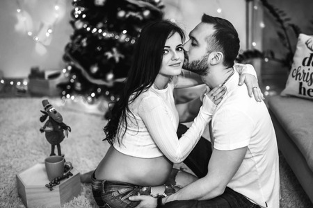 Happy pregnant woman with husband at home with christmas decorationsの写真素材