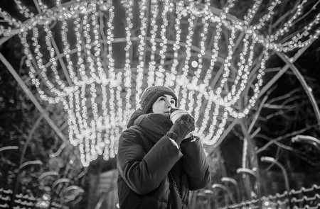 Girl with coffee outdoor in cold weather with christmas lights behindの写真素材