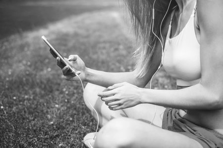 Pretty sporty girl with phone relaxing outdoor after training, black and white