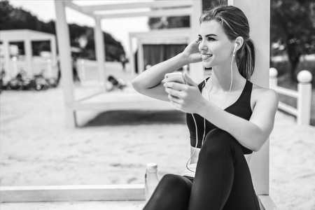 Pretty sporty girl with phone relaxing outdoor after training, black and whiteの写真素材