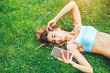 Pretty sporty girl with phone relaxing outdoor after trainingの写真素材