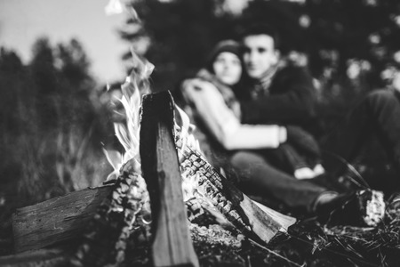 Pretty young couple relaxing near bonfire in the forest at evening timeの写真素材