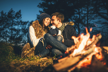 Pretty young couple drinking hot beverage in the forest near bonfireの写真素材