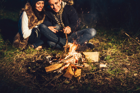 Pretty young couple relaxing near bonfire in the forest at evening timeの写真素材