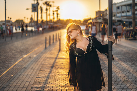 Pretty tourist girl with blond hair in black swimsuit and pareo walking on the bay near seaの写真素材