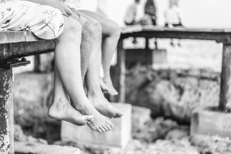 Line of barefoot legs of group of people relaxing on the pier near sea at sunset timeの写真素材