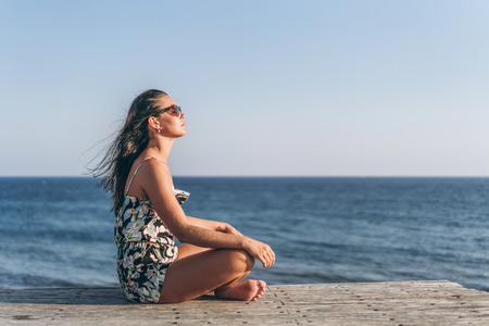 Pretty pan asian girl in dress sitting on the pier near seaの写真素材
